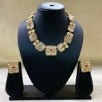 Gold-plated Kundan-style necklace set with central ruby accent and matching square earrings displayed on black stand.