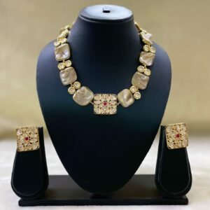 Gold-plated Kundan-style necklace set with central ruby accent and matching square earrings displayed on black stand.
