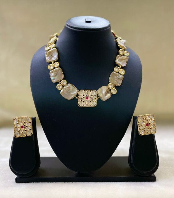 Gold-plated Kundan-style necklace set with central ruby accent and matching square earrings displayed on black stand.