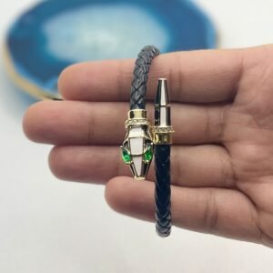 Hand holding a luxury serpent leather bangle with green eyes, gold accents, and braided black strap