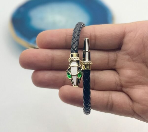 Hand holding a luxury serpent leather bangle with green eyes, gold accents, and braided black strap